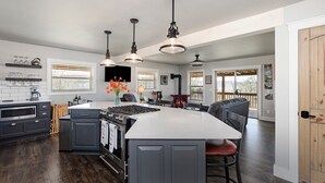 A modern kitchen with a central island, dark cabinetry, and a wood-burning stove. - Eagles Roost.  Wifi & Dog Friendly.  Covered porch & upper Deck w/ Sunset Views (Eagle Rock)