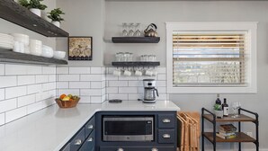 A modern kitchen with white tiles, a coffee maker, a microwave, and a window with blinds. - Eagles Roost.  Wifi & Dog Friendly.  Covered porch & upper Deck w/ Sunset Views (Eagle Rock)