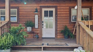 A wooden cabin with a welcoming sign, a front door, and a porch with potted plants. - Eagles Roost.  Wifi & Dog Friendly.  Covered porch & upper Deck w/ Sunset Views (Eagle Rock)