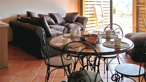 A cozy living area with a sofa, a dining table with chairs, and a view of the outdoors through large windows.