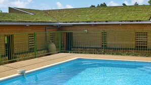 A rectangular swimming pool with a tiled deck area, surrounded by a green metal fence.
