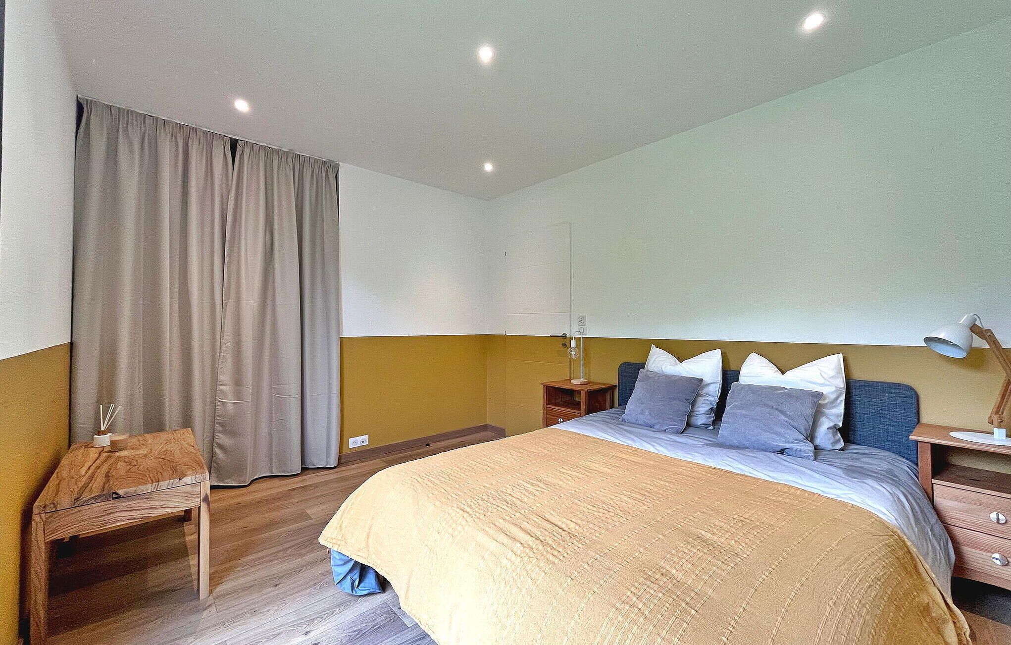 A bedroom with a bed, bedside tables, a desk, a lamp, and a curtain.