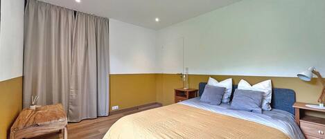 A bedroom with a bed, bedside tables, a desk, a lamp, and a curtain.