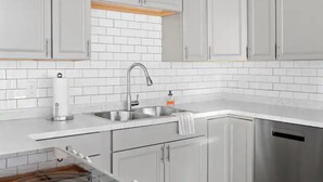 Una cocina moderna con armarios blancos, un lavamanos de acero inoxidable y una encimera de madera.