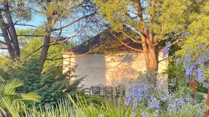 A building with a sloped roof surrounded by lush greenery and flowering plants.