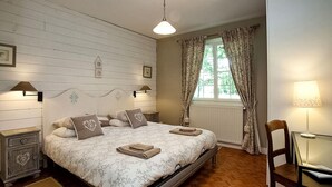 A bedroom with a bed, two bedside tables, a chair, a window with curtains, and a lamp.