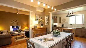 A modern kitchen with a dining area, featuring a long table, chairs, a TV, and a kitchen counter with appliances.