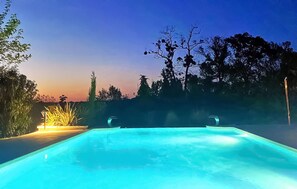 Ein Schwimmbad im Abendlicht, umgeben von Bäumen und bewölktem Himmel.
