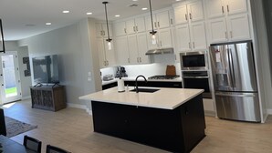 Una cocina moderna con gabinetes blancos, electrodomésticos de acero inoxidable e iluminación colgante.
