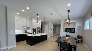 Una cocina moderna con armarios blancos, una isla negra y electrodomésticos de acero inoxidable. Hay un comedor con una mesa y sillas oscuras.