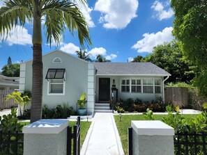 A single-story house with a white exterior, a dark front door, and a small porch. - Northwood Haven (West Palm Beach)