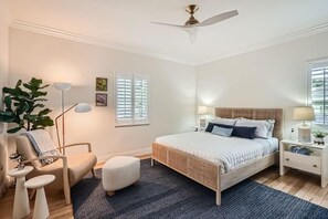 A bedroom with a bed, bedside tables, a floor lamp, a chair, and a large plant. - Northwood Haven (West Palm Beach)