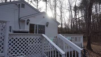 A white wooden cabin with a deck, surrounded by trees.