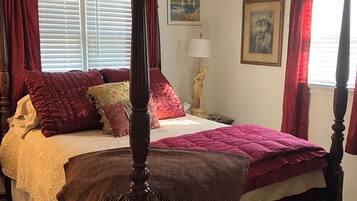 Un lit à baldaquin avec un ventilateur de plafond, des rideaux rouges et deux tableaux encadrés accrochés au mur.