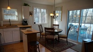 A kitchen with wooden cabinets, a dining area with chairs, a rug, and a chandelier.