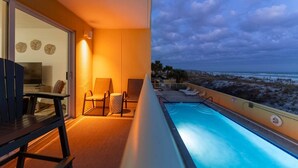 Een balkon met een zwembad, stoelen en uitzicht op het strand in de schemering.