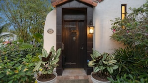 A dark wooden door with a metal handle, flanked by potted plants, and a lit wall-mounted lantern. - Casa Michaeline Vacation Home (West Palm Beach)
