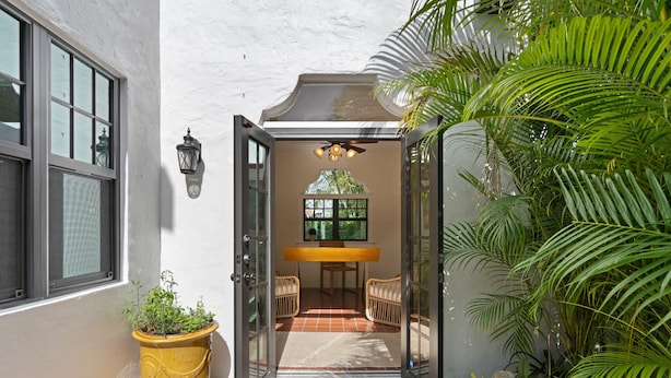 A patio area with a table and chairs, a potted plant, and a view through an open door. - Casa Michaeline Vacation Home (West Palm Beach)