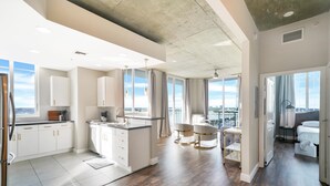 Una cocina moderna con armarios blancos y una isla grande, un comedor con vistas, y un dormitorio con balcón.