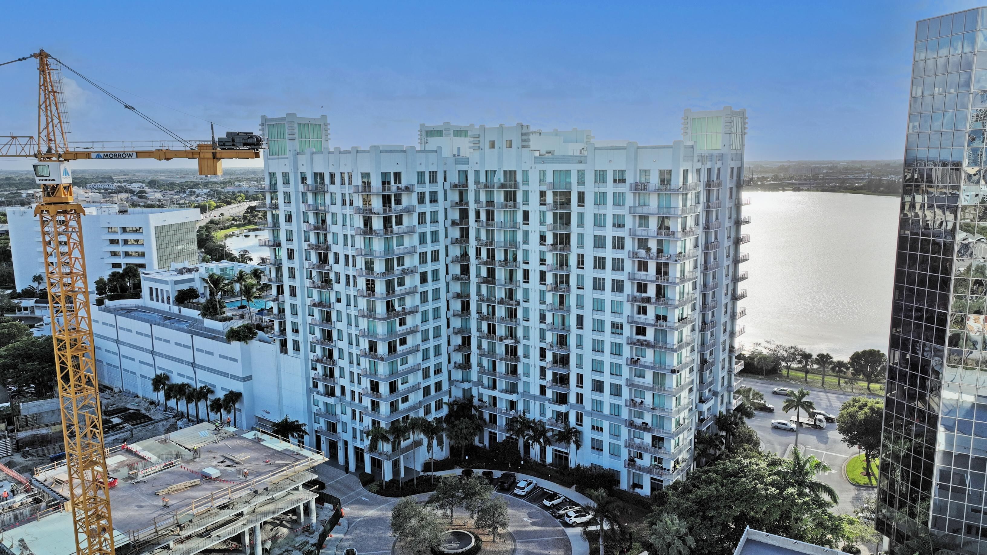 A high-rise building with multiple balconies, a construction crane, and a body of water in the background.