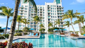 Un hotel con una piscina grande, palmeras y un edificio moderno con balcones.