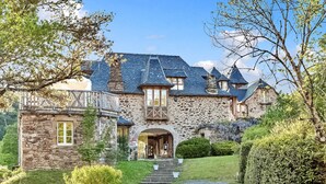 A stone house with a steeply pitched roof, multiple chimneys, and a prominent entrance with steps leading up to it.