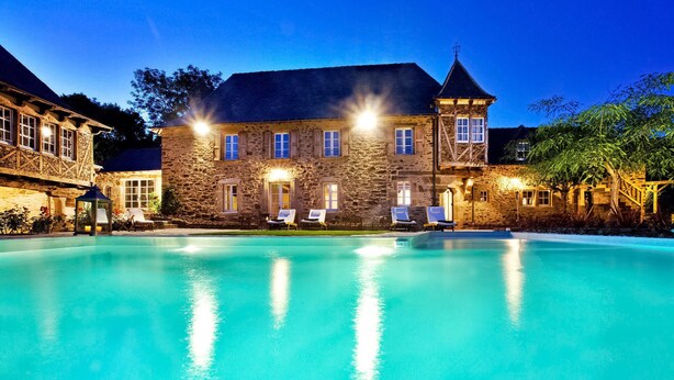 A stone building with a swimming pool, outdoor seating, and a well-lit facade.