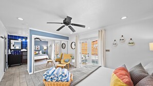 A modern hotel room with a bed, a ceiling fan, a bathroom with a blue tiled wall, and a balcony with a view.
