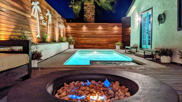 A swimming pool with a fire pit in the center, surrounded by wooden walls and potted plants.