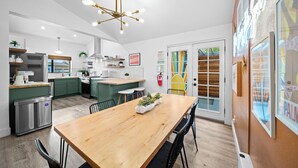 A modern kitchen with a wooden dining table, green cabinets, and a stainless steel refrigerator.
