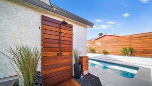 A modern outdoor pool area with a wooden door, potted plants, and a clear blue sky.