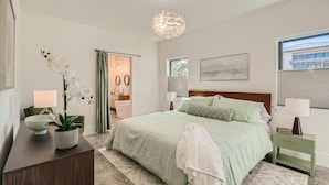 A bedroom with a bed, bedside tables, a potted plant, a lamp, and a view of the outside. - Villa Vogue Vacation Home NEW (West Palm Beach)