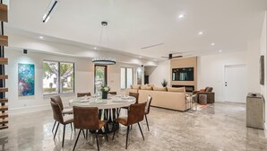 A spacious living area with a round dining table, brown chairs, a beige sofa, and a TV. - Villa Vogue Vacation Home NEW (West Palm Beach)