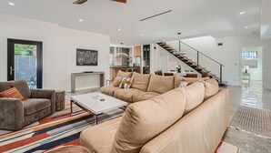 A spacious living area with a large beige sofa, a coffee table, and a TV. There is a staircase leading to an upper level. - Villa Vogue Vacation Home NEW (West Palm Beach)