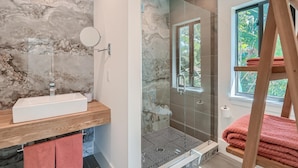 A bathroom with a marble wall, a sink, a mirror, and a shower with a glass door. - Villa Vogue Vacation Home NEW (West Palm Beach)