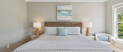 A bedroom with a large bed, two bedside lamps, a wicker headboard, and a painting of the ocean.