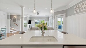 A spacious kitchen with a large island, pendant lighting, and a view to the outside. - 3800 Cameron Boulevard Avantstay Pool, Ocean Views, Deck (Isle of Palms)
