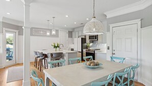 A spacious kitchen with a central island, white cabinetry, and a hanging crystal chandelier. - 3800 Cameron Boulevard Avantstay Pool, Ocean Views, Deck (Isle of Palms)