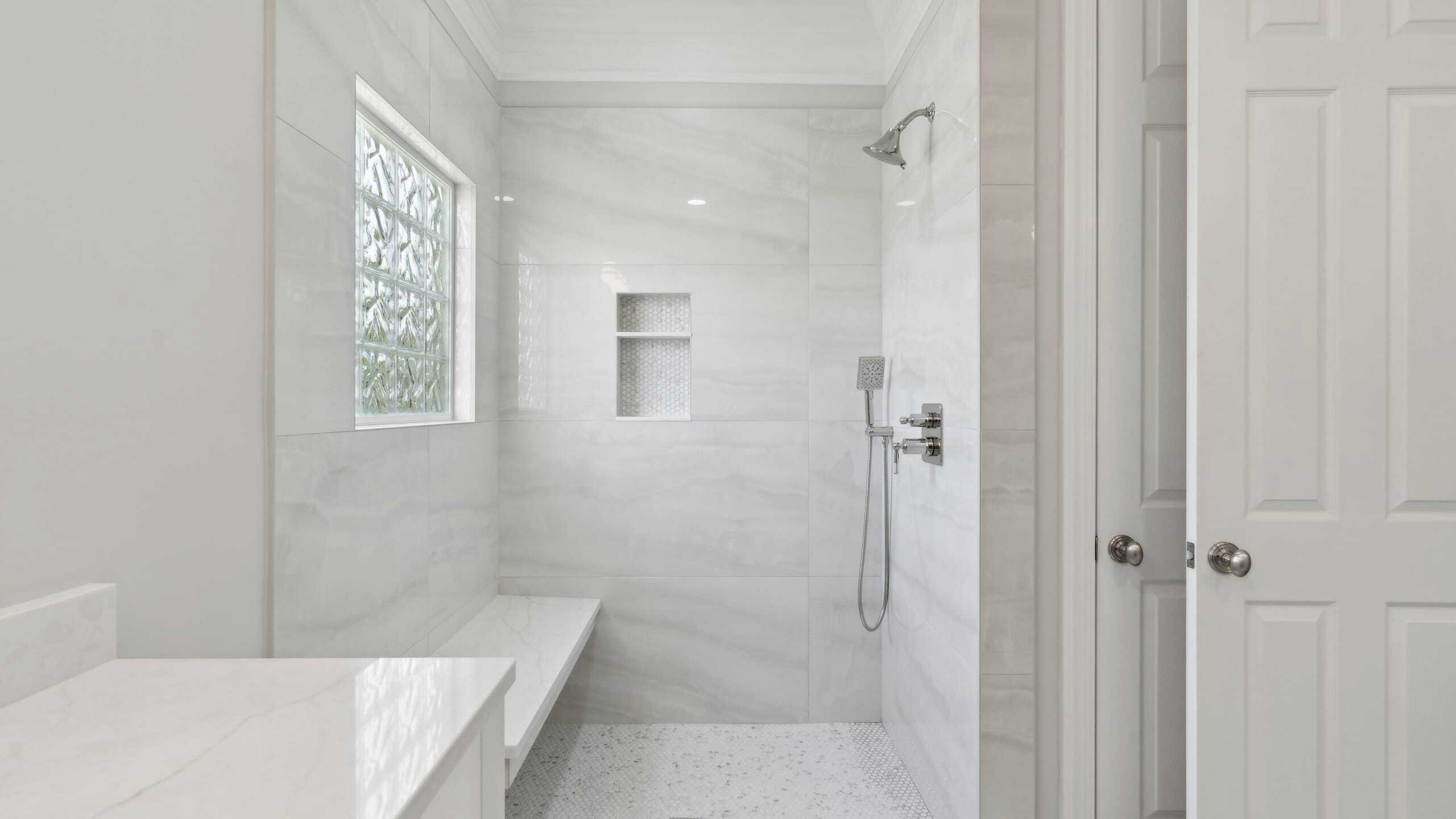 A modern bathroom with a shower, a bench, and a window.
