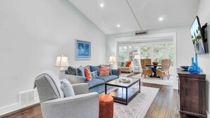 A spacious living room with a grey sofa, a coffee table, and a dining area with wicker chairs. - 17 Sandcrab Court by Avantstay Newly Renovated Home in Beach Town! (Isle of Palms)