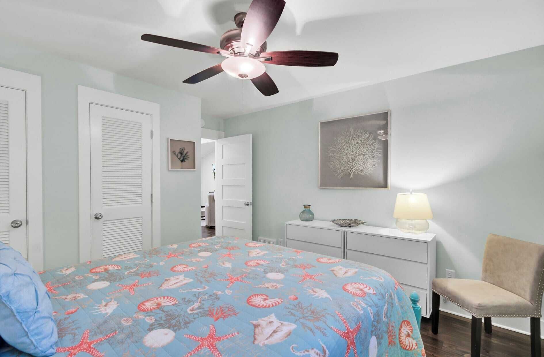 Ein Schlafzimmer mit einem Bett, einem Schreibtisch, einem Stuhl, einem Deckenventilator und einer Wand mit einem gerahmten Bild.