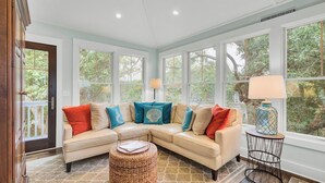 A cozy living room with a sectional sofa, a lamp, and large windows. - 17 Sandcrab Court by Avantstay Newly Renovated Home in Beach Town! (Isle of Palms)
