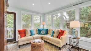 A cozy living room with a sectional sofa, a lamp, and large windows. - 17 Sandcrab Court by Avantstay Newly Renovated Home in Beach Town! (Isle of Palms)