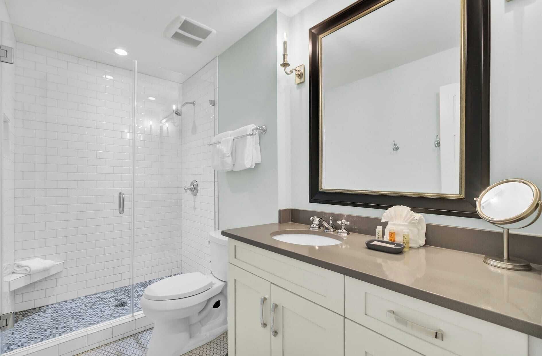 A modern bathroom with a glass-enclosed shower, a white toilet, a vanity with a mirror, and a sink.