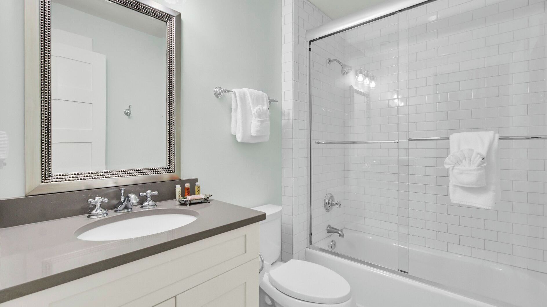 Un baño con lavamanos doble, inodoro, ducha con puertas de vidrio y un espejo grande con marco decorativo.