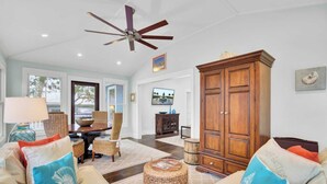 A spacious living room with a ceiling fan, a dining area with wicker furniture, and a large wooden cabinet. - 17 Sandcrab Court by Avantstay Newly Renovated Home in Beach Town! (Isle of Palms)
