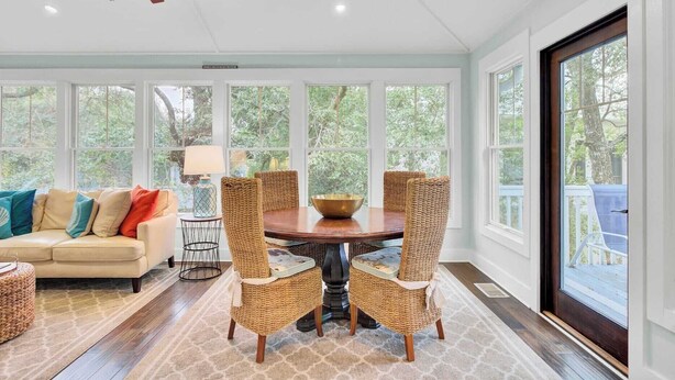 A sunroom with a ceiling fan, wicker chairs, a round table, and a sofa with cushions. - 17 Sandcrab Court by Avantstay Newly Renovated Home in Beach Town! (Isle of Palms)