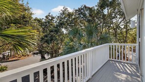A wooden deck with a white railing, surrounded by various trees and plants. - 12 Dunecrest Lane by Avantstay 2 Mins to Beach w/ Pool & BBQ (Isle of Palms)