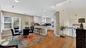 A modern kitchen with white cabinets, a central island, and a dining area with a colorful rug. - 12 Dunecrest Lane by Avantstay 2 Mins to Beach w/ Pool & BBQ (Isle of Palms)