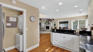 A kitchen with white cabinets, a black countertop, and a wooden floor. - 12 Dunecrest Lane by Avantstay 2 Mins to Beach w/ Pool & BBQ (Isle of Palms)